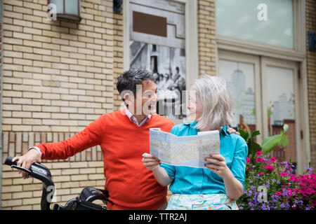 Happy mature couple reading road map debout avec location à l'extérieur du bâtiment Banque D'Images