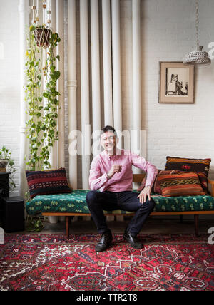 Full Length portrait of smiling man sitting on chaise longue à la maison Banque D'Images