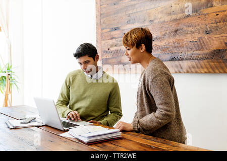 Des collègues masculins et féminins à l'aide d'ordinateur portable à la table dans creative office Banque D'Images