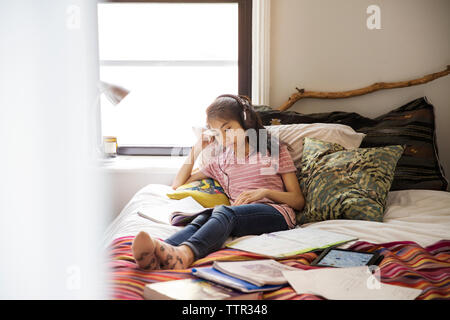 Teenage girl with headphones leurs études tout en sitting on bed Banque D'Images