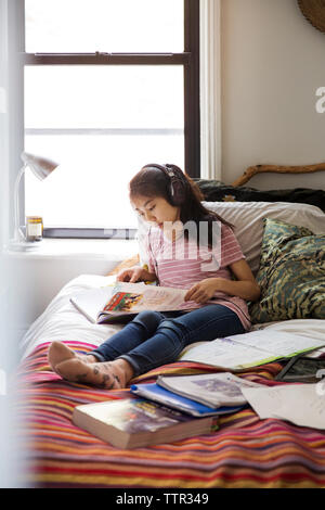 Teenage girl studying with headphones on bed at home Banque D'Images