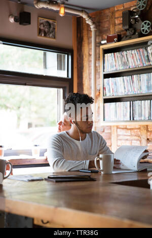 L'homme écoute de la musique pendant la lecture réserve en cafe Banque D'Images