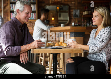 Les gens parler tout en ayant le café et croissants à table in cafe Banque D'Images