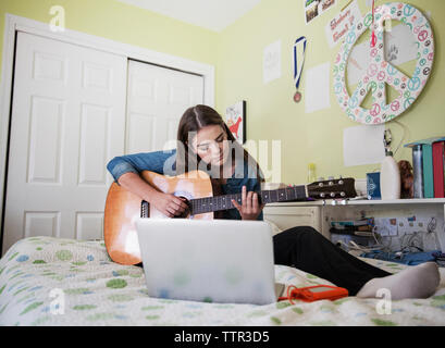 Woman practicing guitar while sitting par laptop at home Banque D'Images