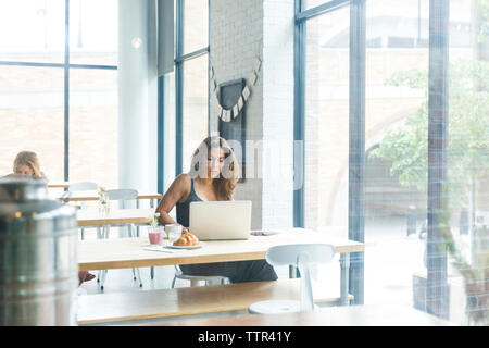 Woman while sitting in cafe avec ami en arrière-plan de la fenêtre vu par Banque D'Images