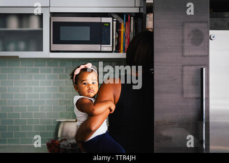 Vue arrière du mère portant mignon fille debout dans la cuisine à la maison Banque D'Images