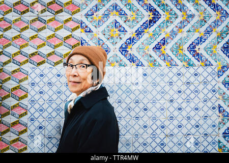 Portrait of senior woman wearing vêtements chauds contre le mur carrelé de couleur permanent en ville Banque D'Images