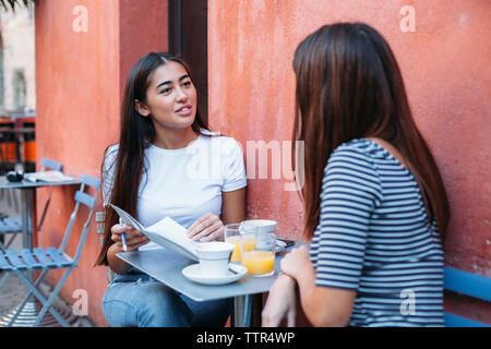 Femme amis parler assis at sidewalk cafe Banque D'Images