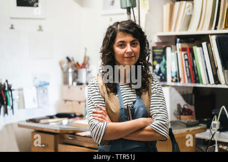 Portrait of female artist with arms crossed standing contre des étagères dans l'atelier Banque D'Images