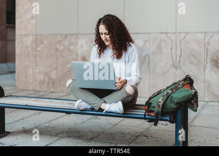 Jeune femme à l'aide de l'ordinateur portable sur le banc Banque D'Images