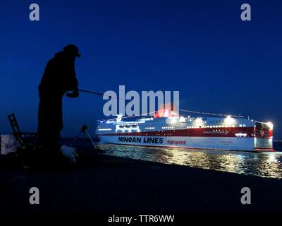 Silhouette d'un homme de la jetée de pêche d'un navire sortant de la Minoan Lines Harbour dans l'arrière-plan. Héraklion, Crète, Grèce. Banque D'Images