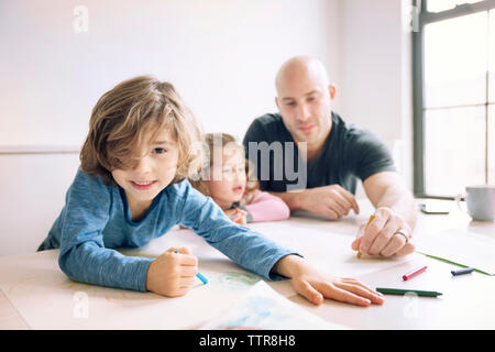 Portrait of boy drawing tout en aidant père fille at home Banque D'Images