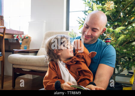 Heureux père regardant son fils habillé en costume contre le sapin de noël à la maison Banque D'Images