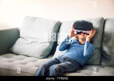 Happy boy wearing simulateur de réalité virtuelle sitting on sofa at home Banque D'Images