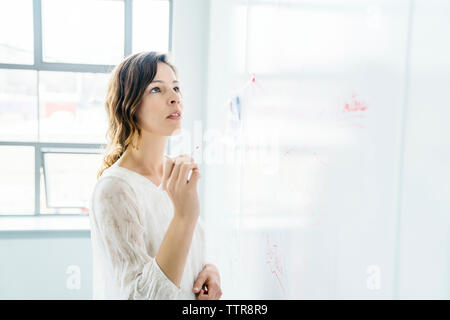 Vue de côté businesswoman writing on whiteboard in office Banque D'Images