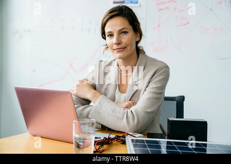 Portrait of businesswoman with arms crossed assis contre l'office Banque D'Images