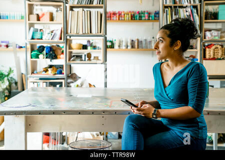 Thoughtful businesswoman using smart phone while sitting in office Banque D'Images