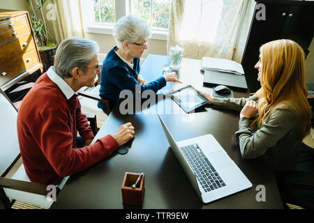 Portrait de conseiller financier expliquant plan pour senior couple on tablet computer in office Banque D'Images