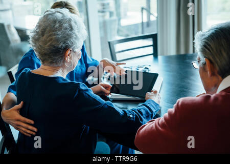 Aide familiale au cours de l'ordinateur tablette avec senior couple assis à table à manger Banque D'Images