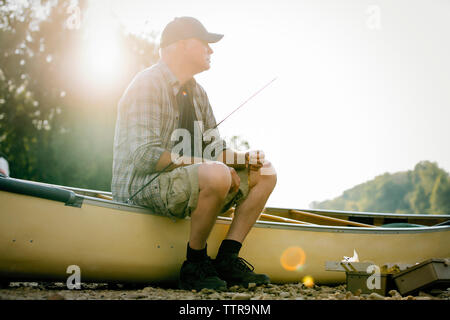 Happy man sitting on boat au lakeshore contre ciel clair Banque D'Images