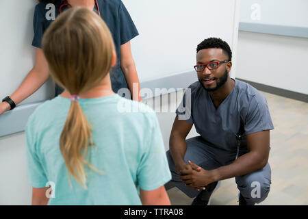 Pédiatre de parler avec girl alors que crouching par collègue in hospital corridor Banque D'Images