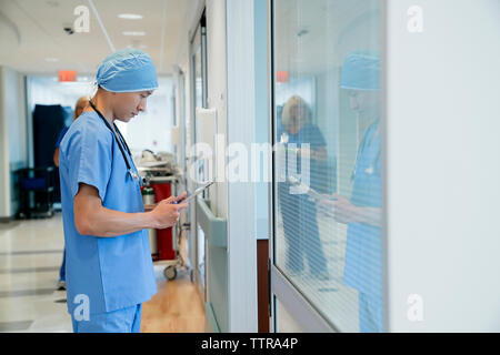 Chirurgien using tablet computer while standing in hospital corridor Banque D'Images