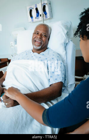 Heureux père parler avec sa fille tout en s'appuyant sur bed in hospital ward Banque D'Images