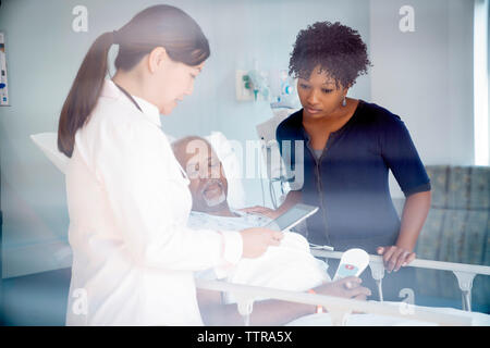 Femme médecin montrant tablet computer to senior patient in hospital ward femme et vu à travers la vitre Banque D'Images