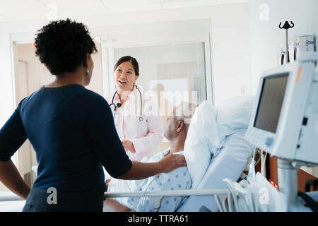 Doctor talking with woman standing by father in hospital ward Banque D'Images