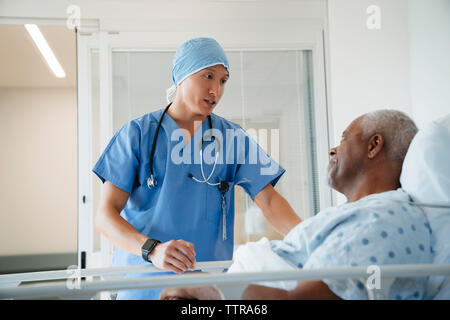 Chirurgien sérieux talking with senior patient lying on bed in hospital ward Banque D'Images