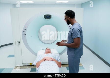 Vue latérale d'infirmier parle avec patient couché pour l'IRM dans la salle d'examen Banque D'Images