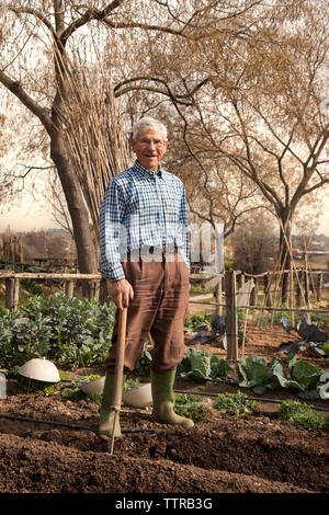 Portrait of senior farmer holding de l'outil de travail en se tenant sur le terrain Banque D'Images