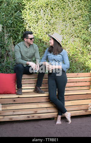 Couple holding beer bottles parler tout en vous relaxant sur banc en bois dans la cour Banque D'Images