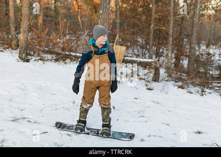 Snowboard garçon sur le terrain couvert de neige dans la forêt Banque D'Images