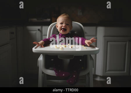 Portrait of cute baby girl crying, assis sur une chaise haute dans la cuisine à la maison Banque D'Images