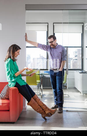 Happy businesswoman discussing over tablet computer with male colleague in creative office