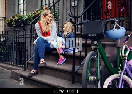 Happy mother and daughter talking while sitting on steps Banque D'Images