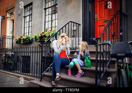 Mère ludique holding cookies en face des yeux alors qu'il était assis avec sa fille sur les mesures Banque D'Images