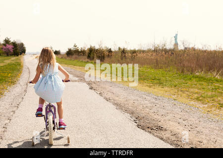 Vue arrière du girl riding vélo sur route au milieu de terrain Banque D'Images