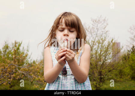 Cute girl blowing dandelion sur terrain contre ciel clair Banque D'Images