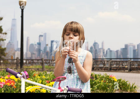 Cute girl blowing dandelion sur promenade avec ville en arrière-plan Banque D'Images