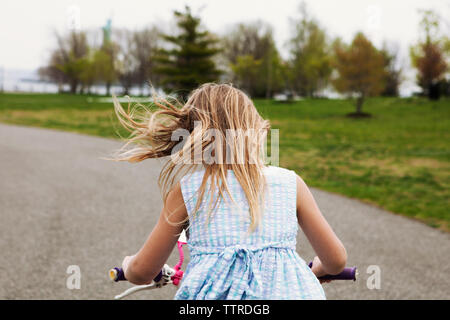 Vue latérale du girl riding vélo sur route par domaine Banque D'Images