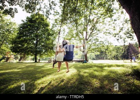 Vue arrière du sisters sitting on swing à grass field Banque D'Images