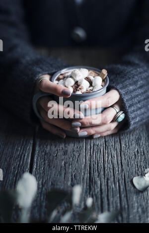 Portrait de femme tenant une tasse de chocolat chaud avec des guimauves à table en bois Banque D'Images