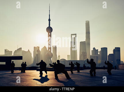 Silhouette des gens pratiquant le karaté sur terrasse de l'immeuble contre skyscrapers in city pendant le coucher du soleil Banque D'Images