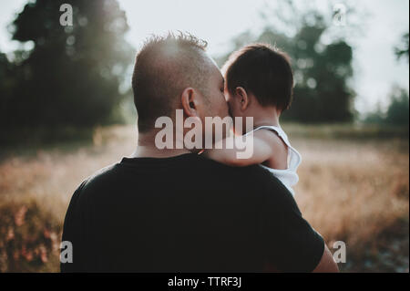 Vue arrière du kissing son père en se tenant sur le terrain herbeux Banque D'Images