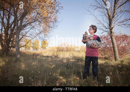 Boy carrying dog en se tenant sur le terrain herbeux contre clear sky at park Banque D'Images