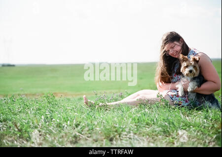 La longueur totale de l'excès de teenage girl Playing with Yorkshire Terrier on grassy field contre ciel clair au cours de journée ensoleillée Banque D'Images