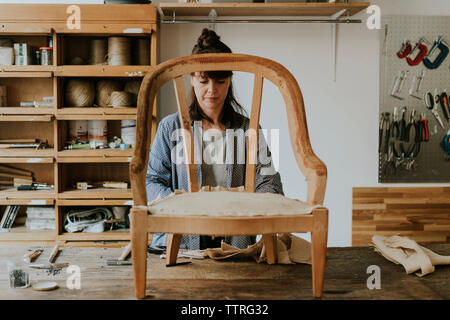 Confident female tapissier avec chaise en bois sur la table debout dans l'atelier Banque D'Images