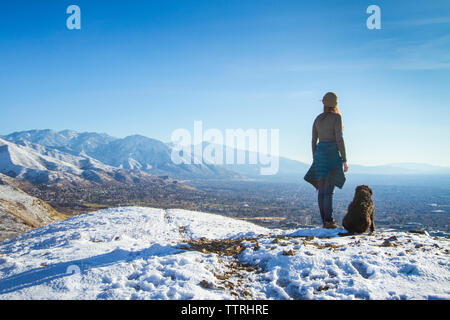 Rear view of woman with dog standing on mountain contre le ciel au cours de l'hiver Banque D'Images